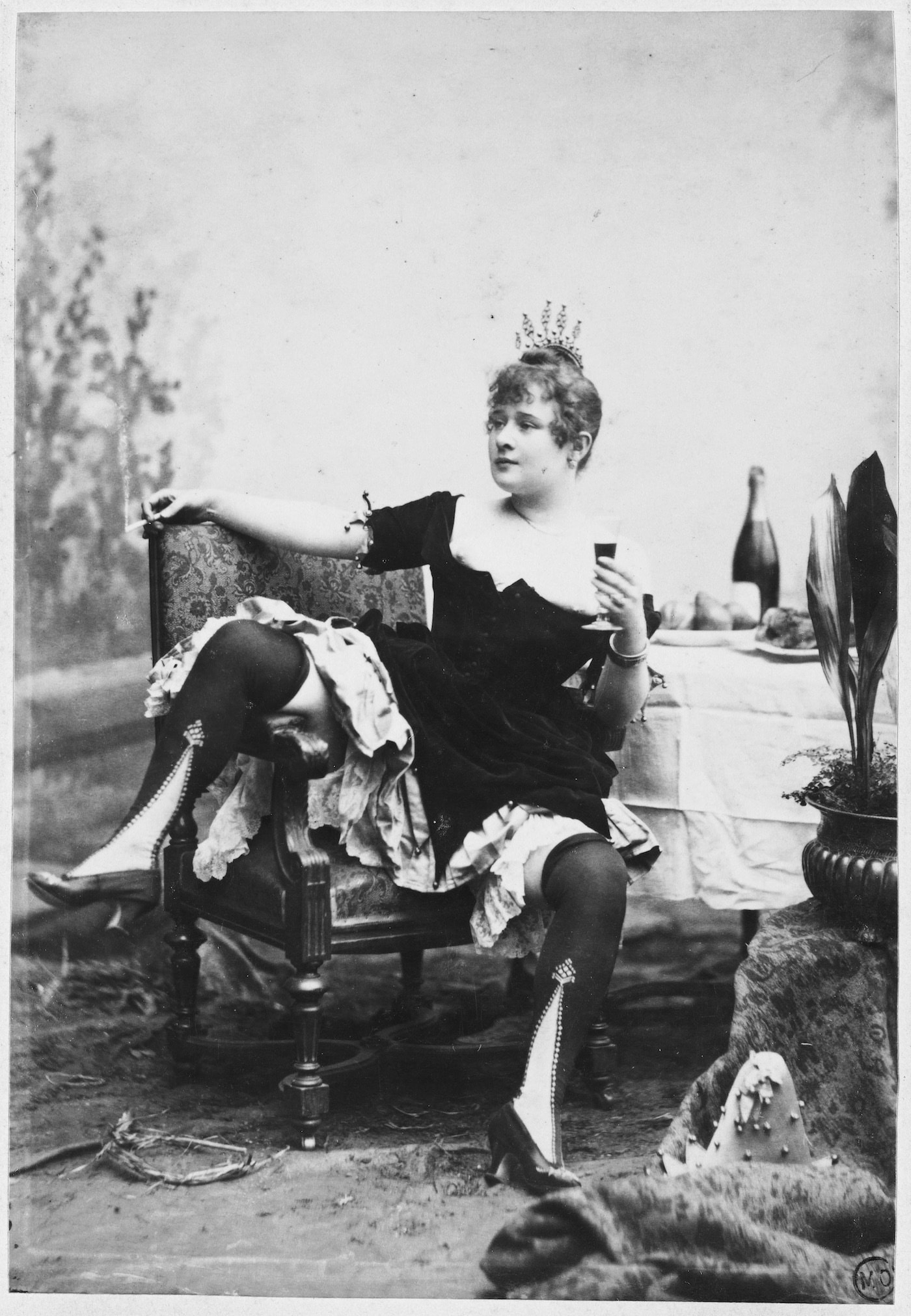 La Goulue assise sur une chaise, jambes ÈcartÈes, tenant une cigarette à la main droite et un verre de vin la main gauche. Vers 1885